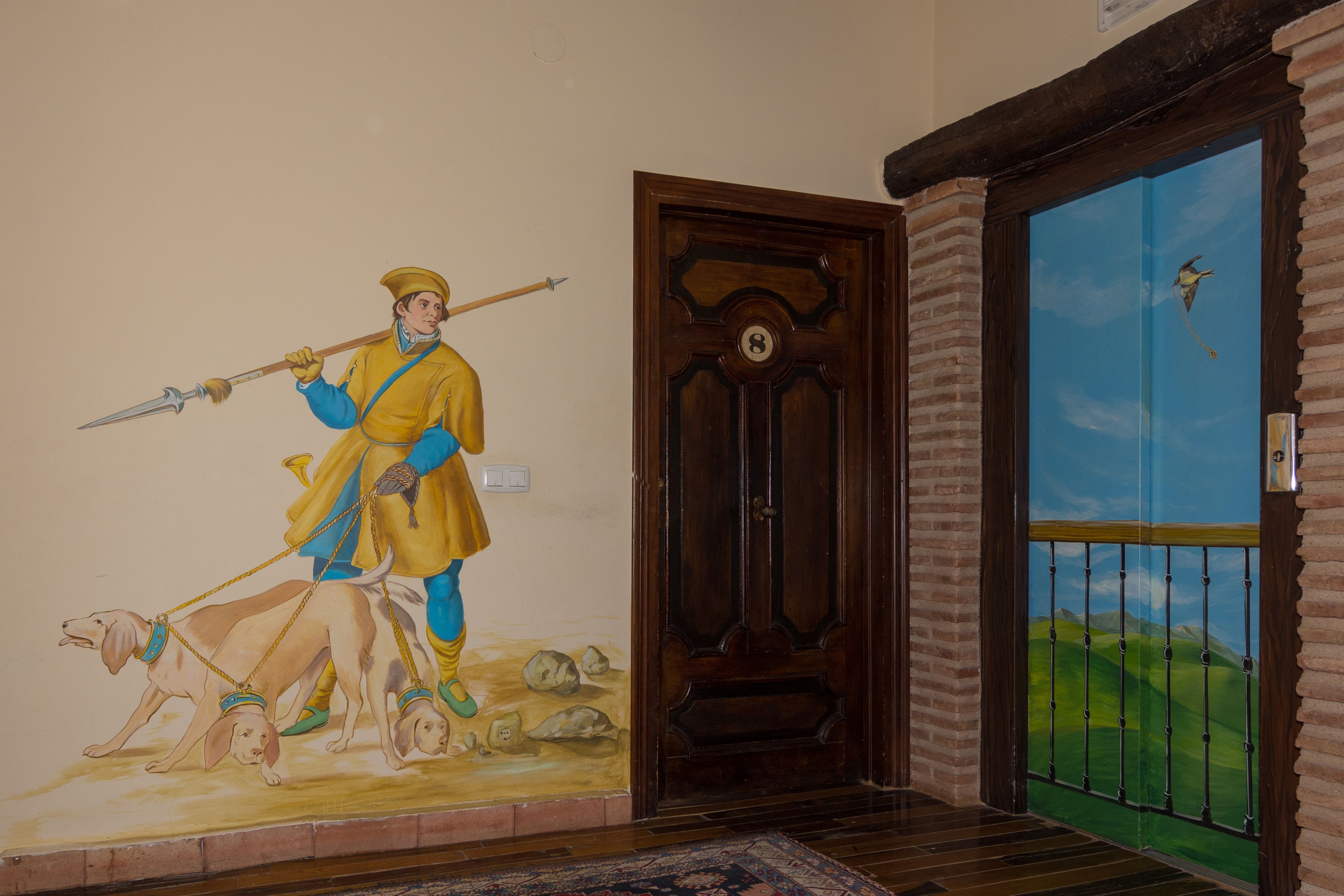 Un mural de una figura histórica con perros, una puerta de madera y una vista de un paisaje verde a través de una puerta de cristal.