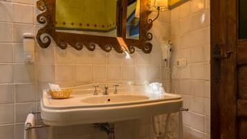 Un baño con un lavamanos blanco, dos lámparas de pared, un espejo con marco decorativo y una puerta de madera.