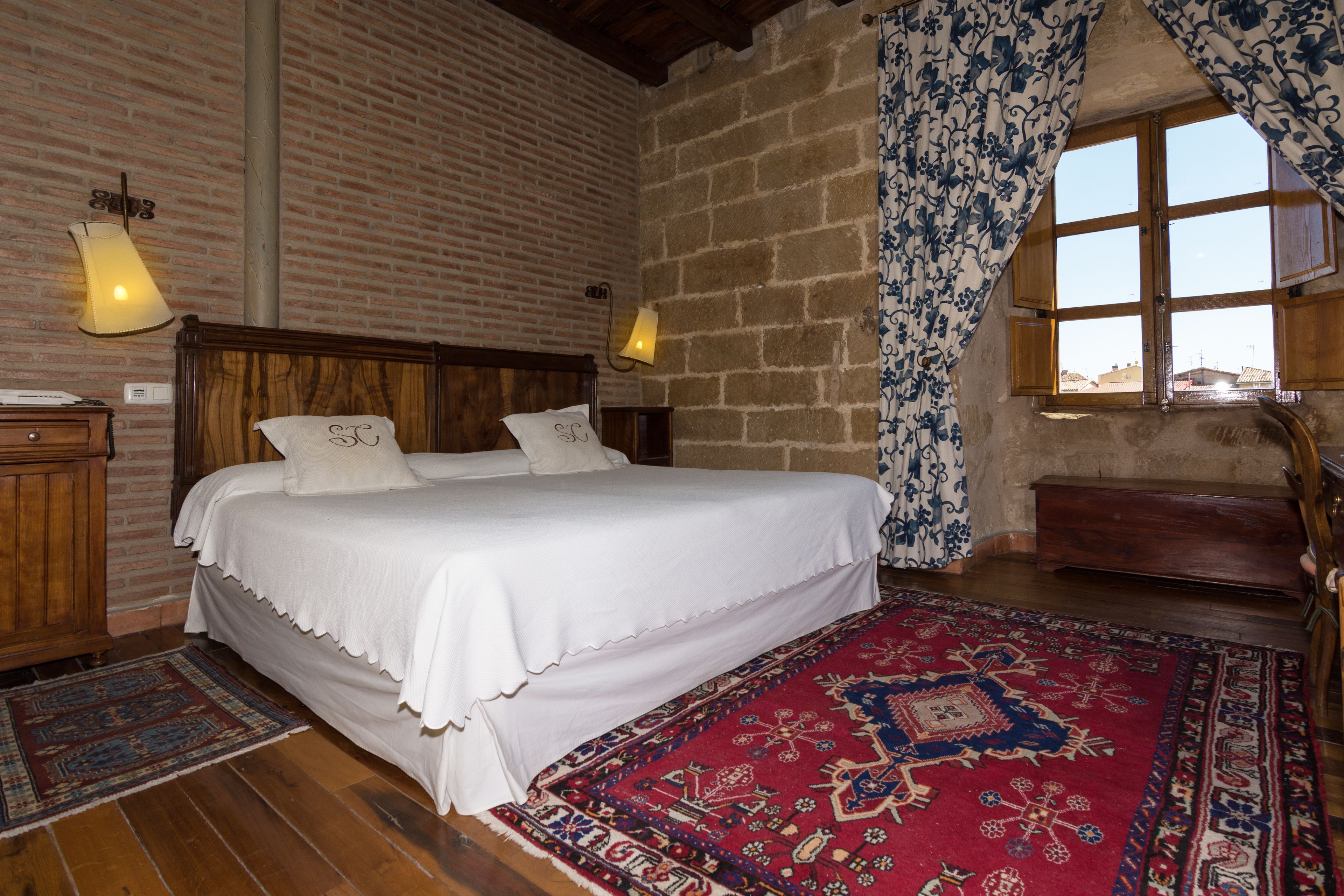Ein Schlafzimmer mit einem hölzernen Bett, einem Teppich mit rotem Muster und einer Ziegelwand.
