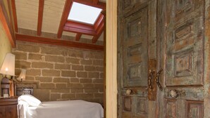 A bedroom with a wooden floor, a bed, a nightstand, a lamp, a window, and a large wooden door. - Hospedería Señorío de Casalarreina (Casalarreina)