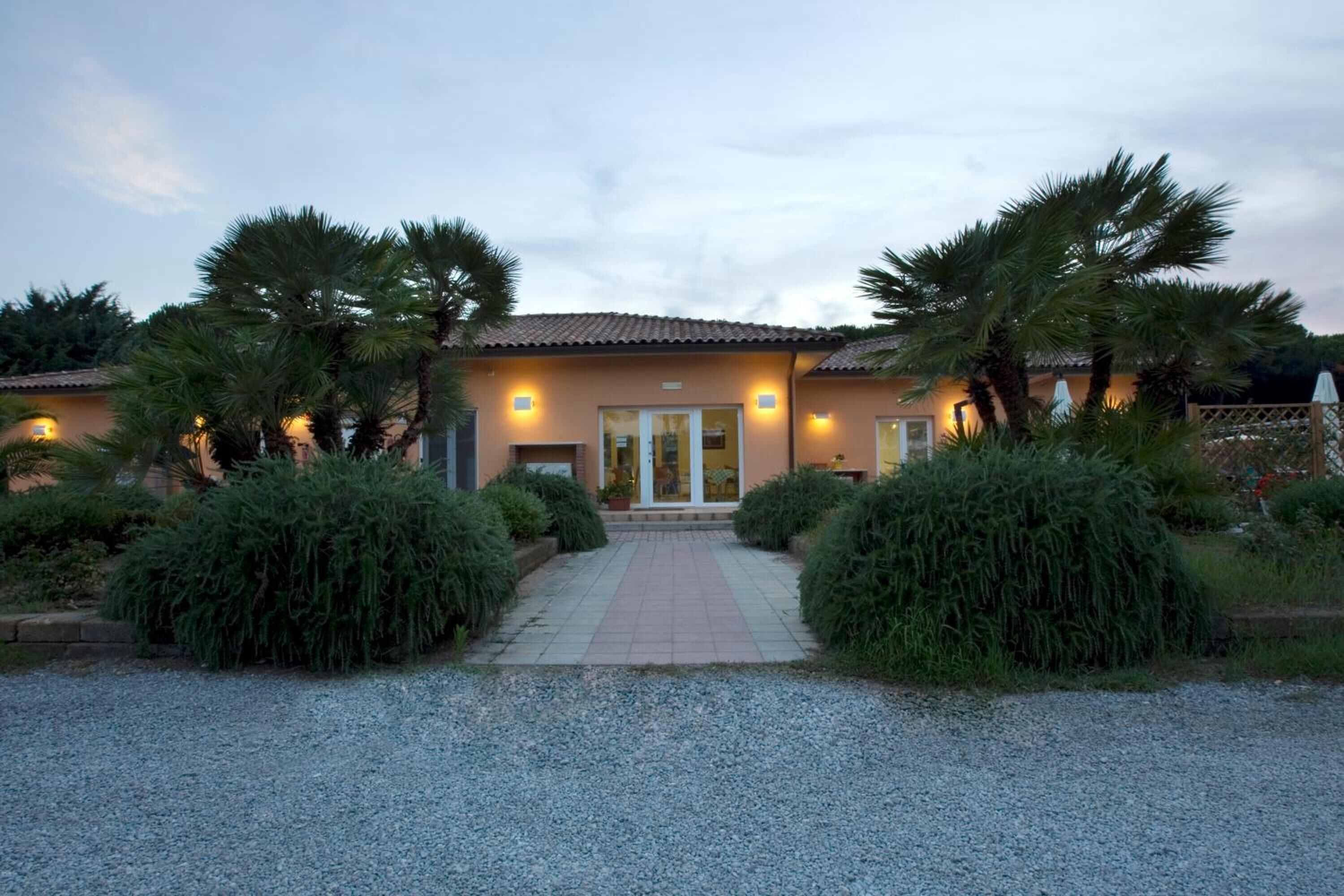 Un edificio con tetto in tegole, vialetto sterrato e un sentiero che conduce all'ingresso.