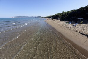 A beach with clear water, a sandy shore, and a few beach chairs. - Hotel Le Palme (Orbetello)