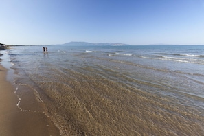 Une plage aux eaux claires et peu profondes, avec une chaîne de montagnes visible au loin.