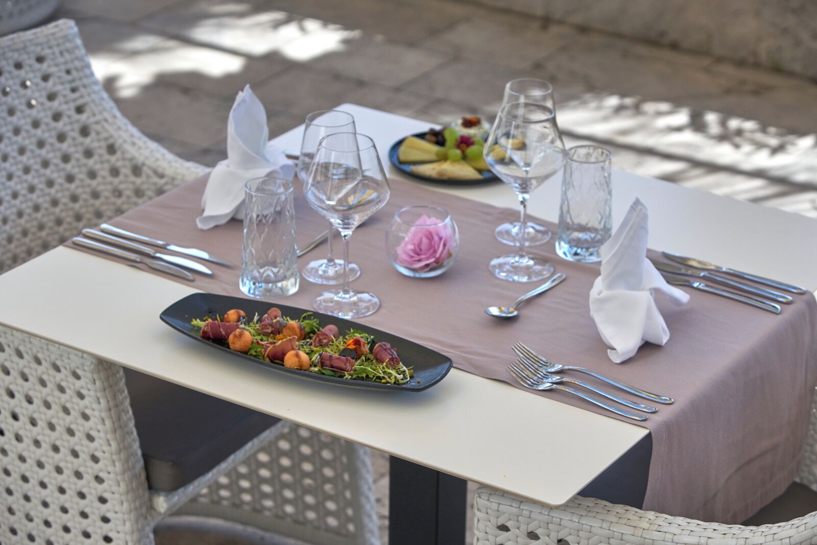 Una mesa de comedor al aire libre con un plato de comida, copas de vino y cubiertos.