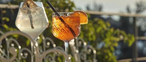 Two cocktails on a table with a metal railing and greenery in the background.