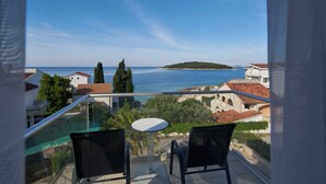 A balcony with two chairs and a small table, overlooking a coastal view with buildings and a distant island. - Boutique Hotel Life (Rogoznica)