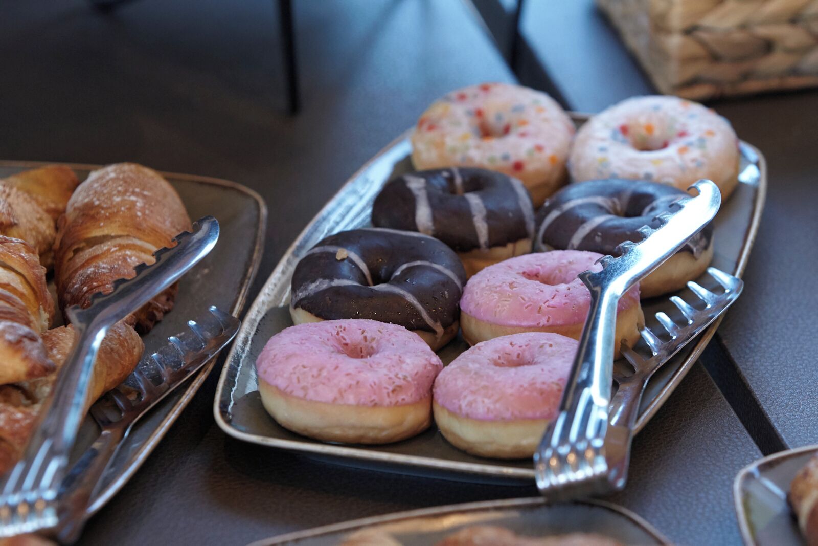 Bandeja con varios pasteles, incluyendo croissants y donas, junto con unas pinzas.