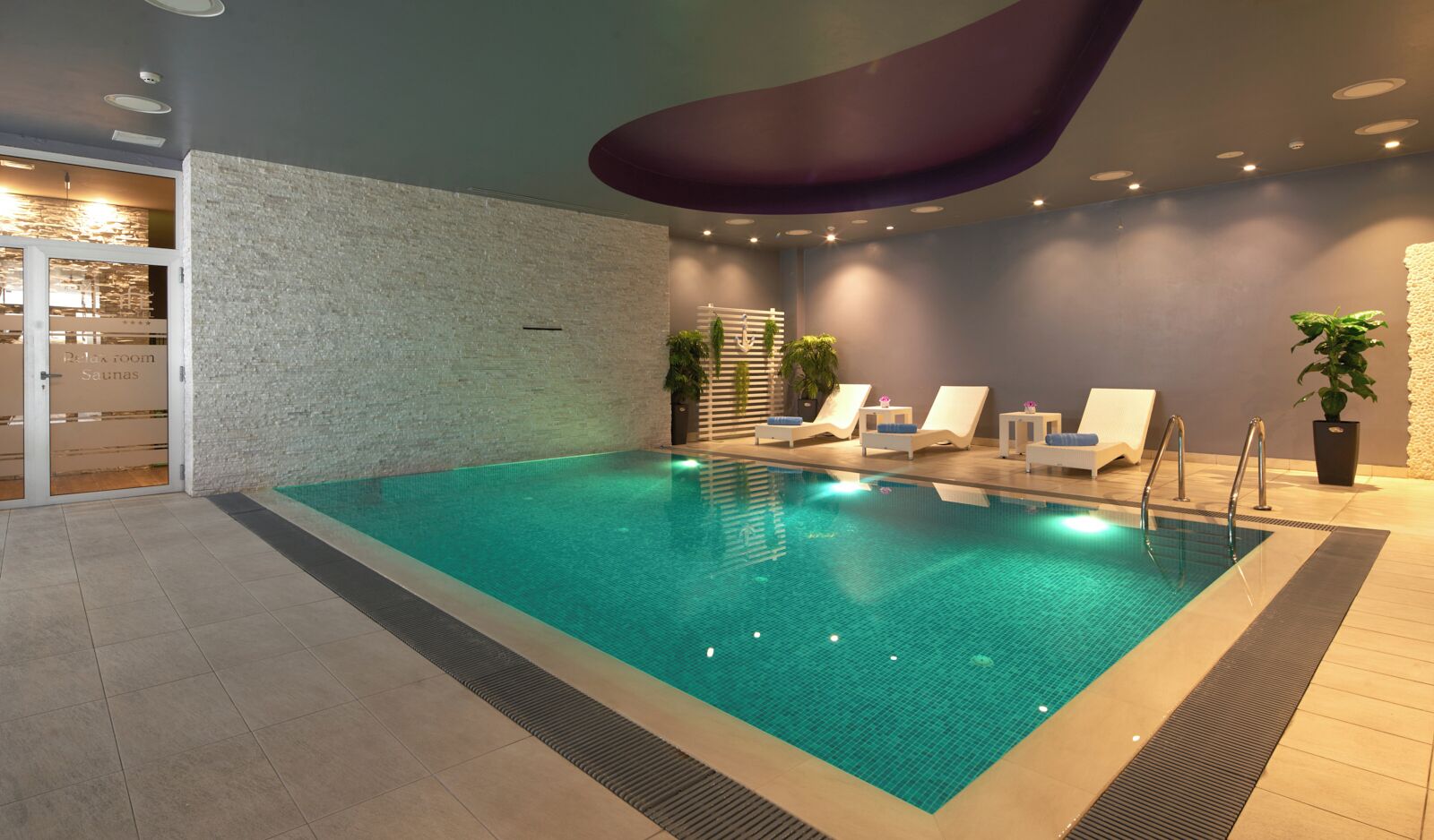 An indoor swimming pool with lounge chairs and a spa area.