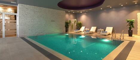 An indoor swimming pool with lounge chairs and a spa area.
