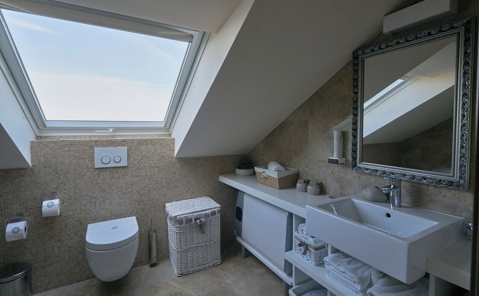 A modern bathroom with a skylight, a toilet, a sink, and a large mirror.