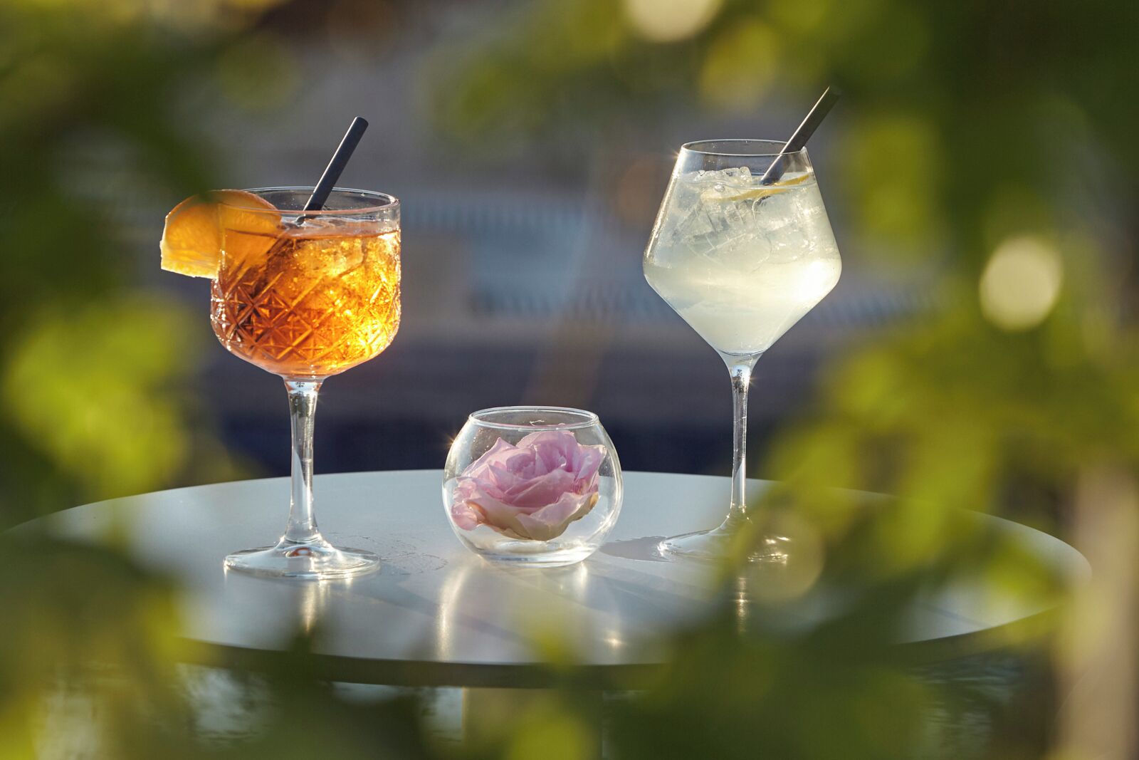 Two cocktails on a table with a glass of flowers.