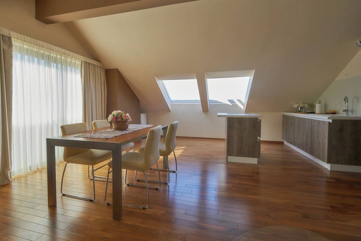 A spacious loft with a dining area, a kitchenette, and large windows.