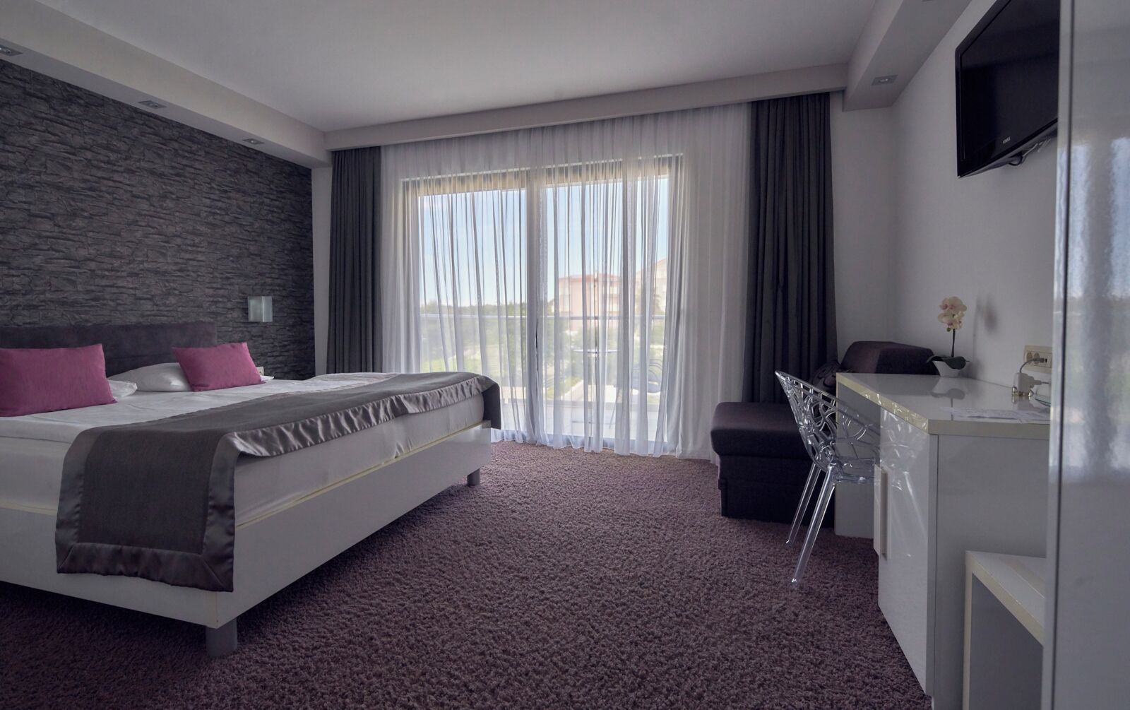 A modern hotel room with a large bed, a desk, and a view of the outdoors.