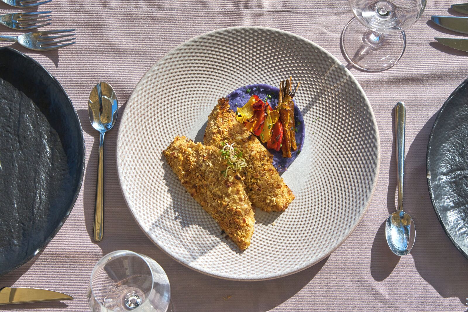 A dining table with a plate of food, cutlery, and glasses.