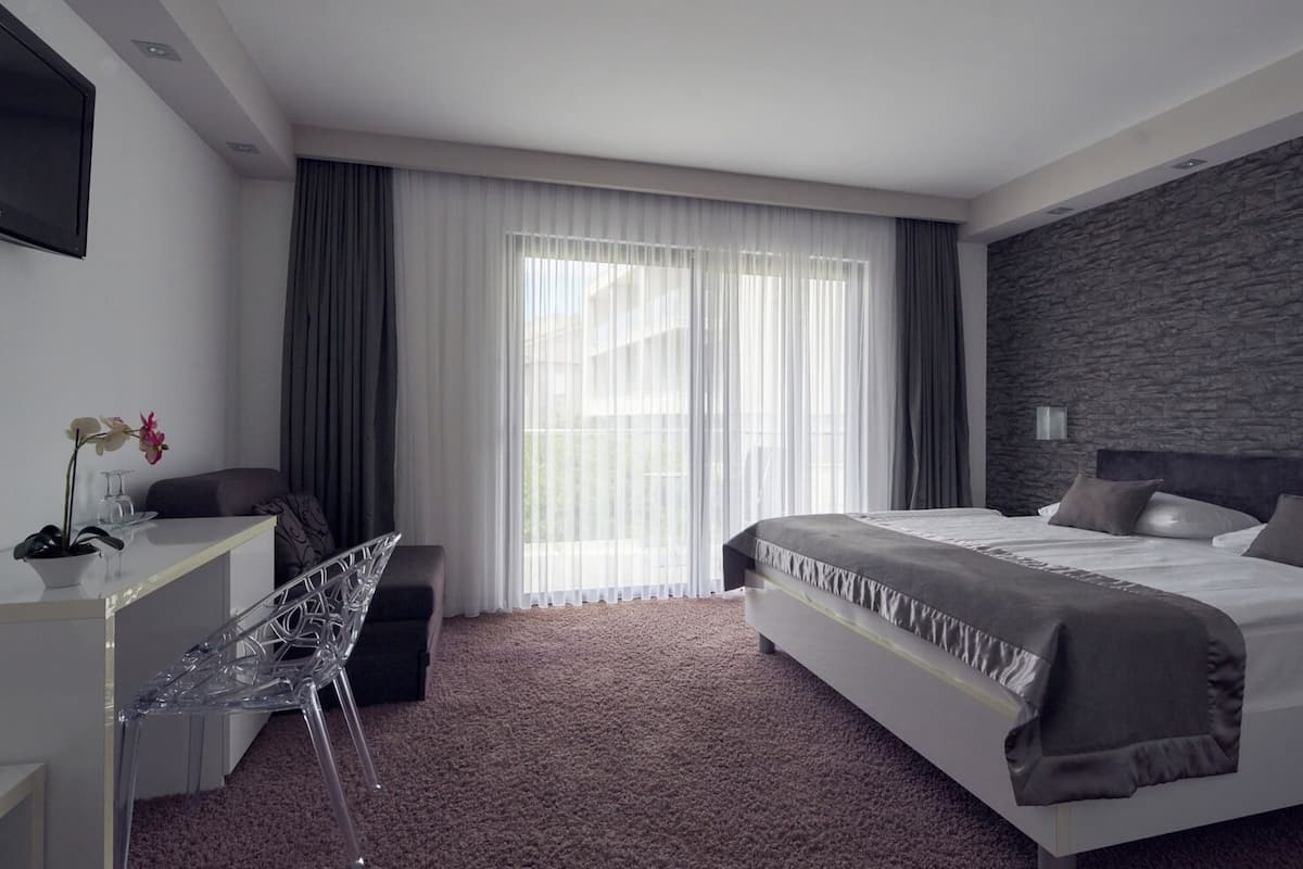 A modern hotel room with a large bed, a desk with a chair, and a stone accent wall.