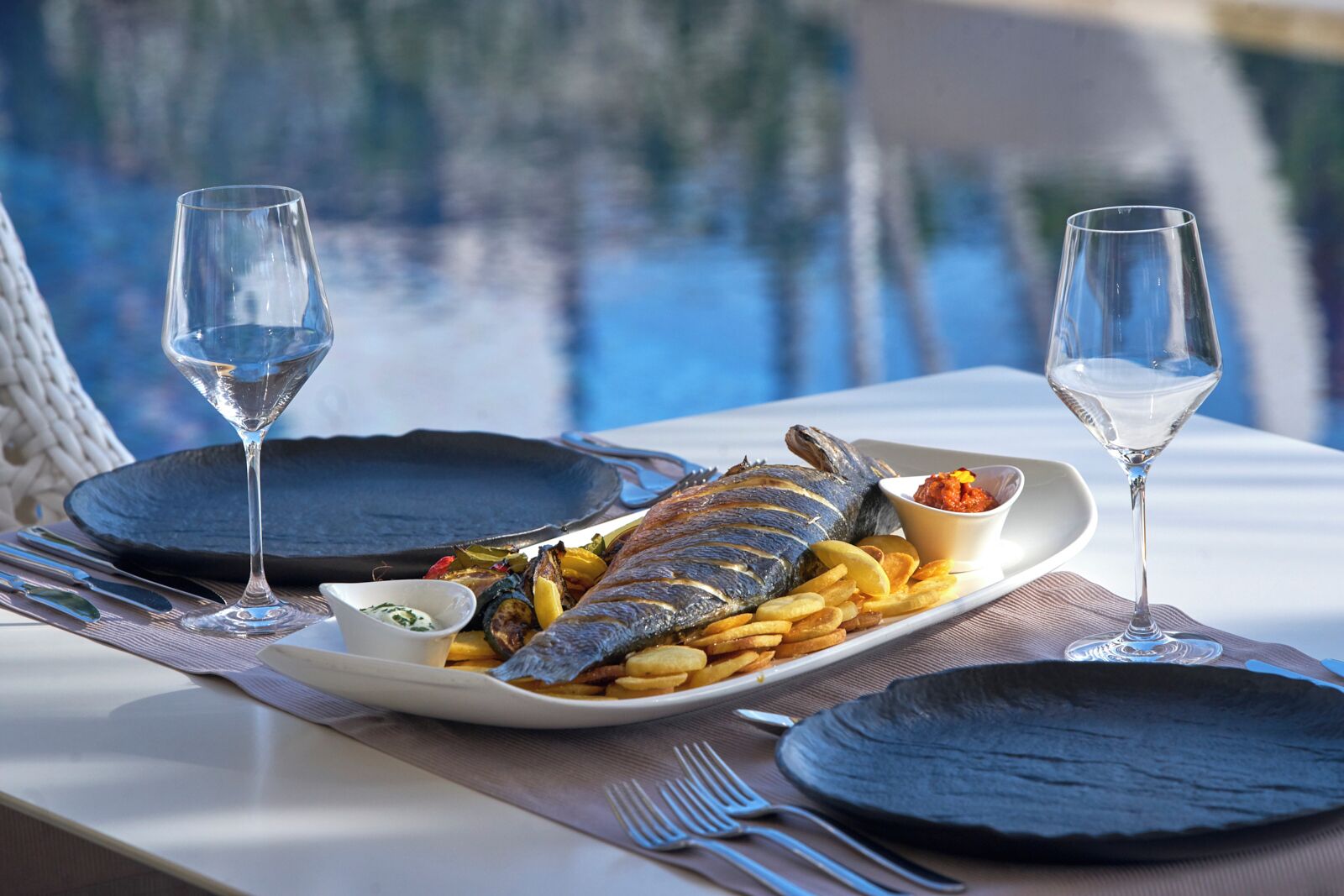 Una mesa con un plato de pescado, papas fritas y dos vasos de agua.