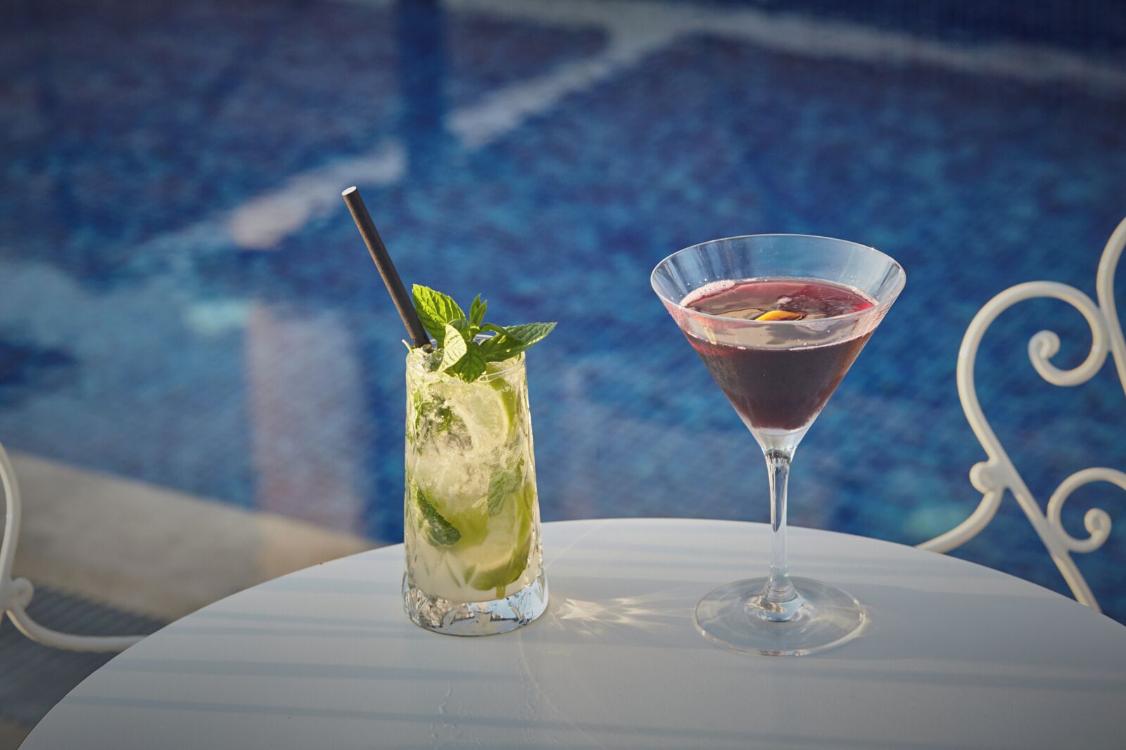 Two drinks on a table by a poolside.