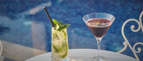 Two drinks on a table by a poolside.
