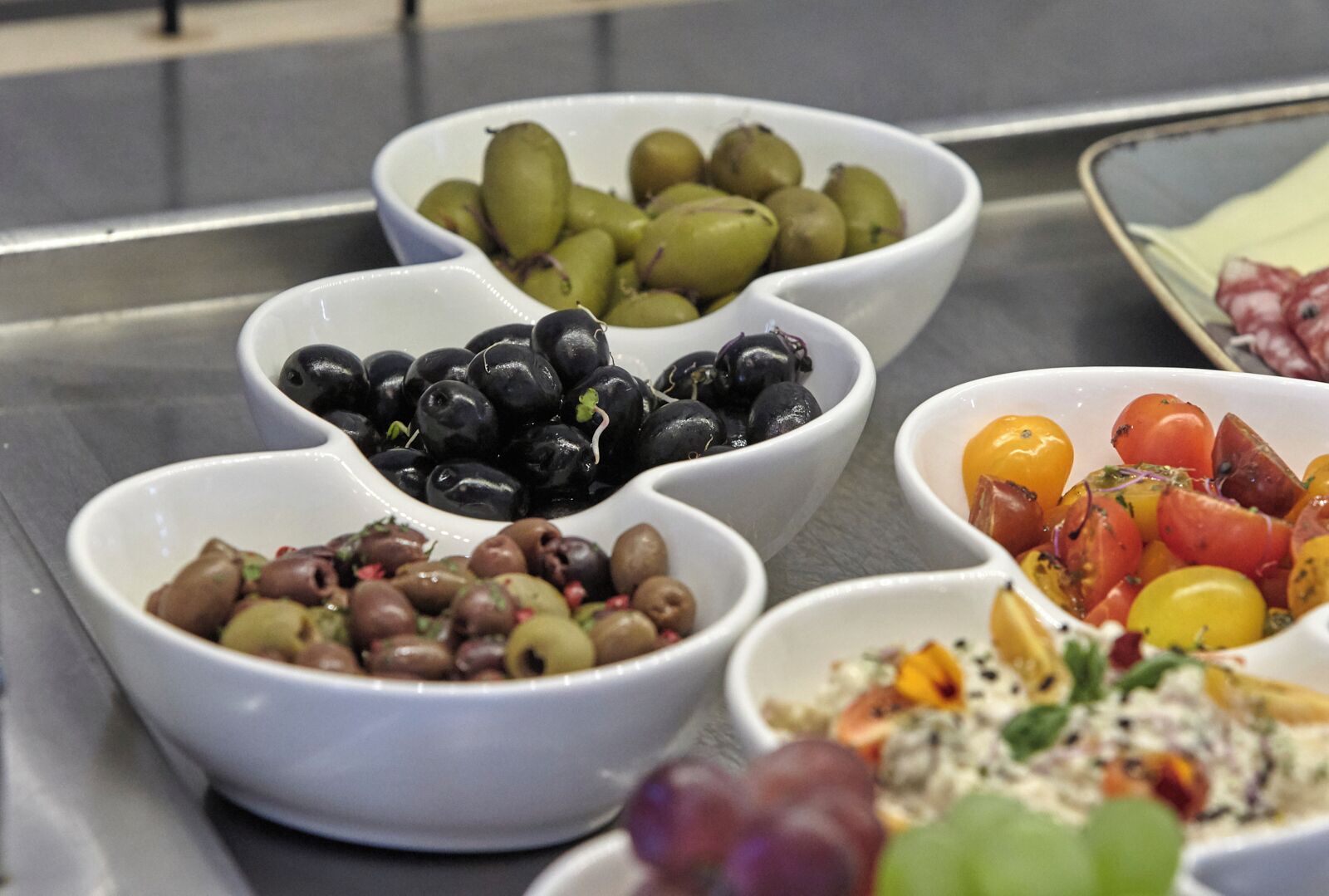 A buffet with various dishes including olives, tomatoes, and grapes.