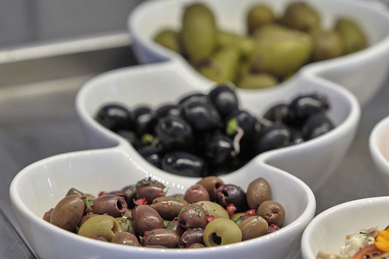 Three white bowls containing olives and pomegranate seeds.