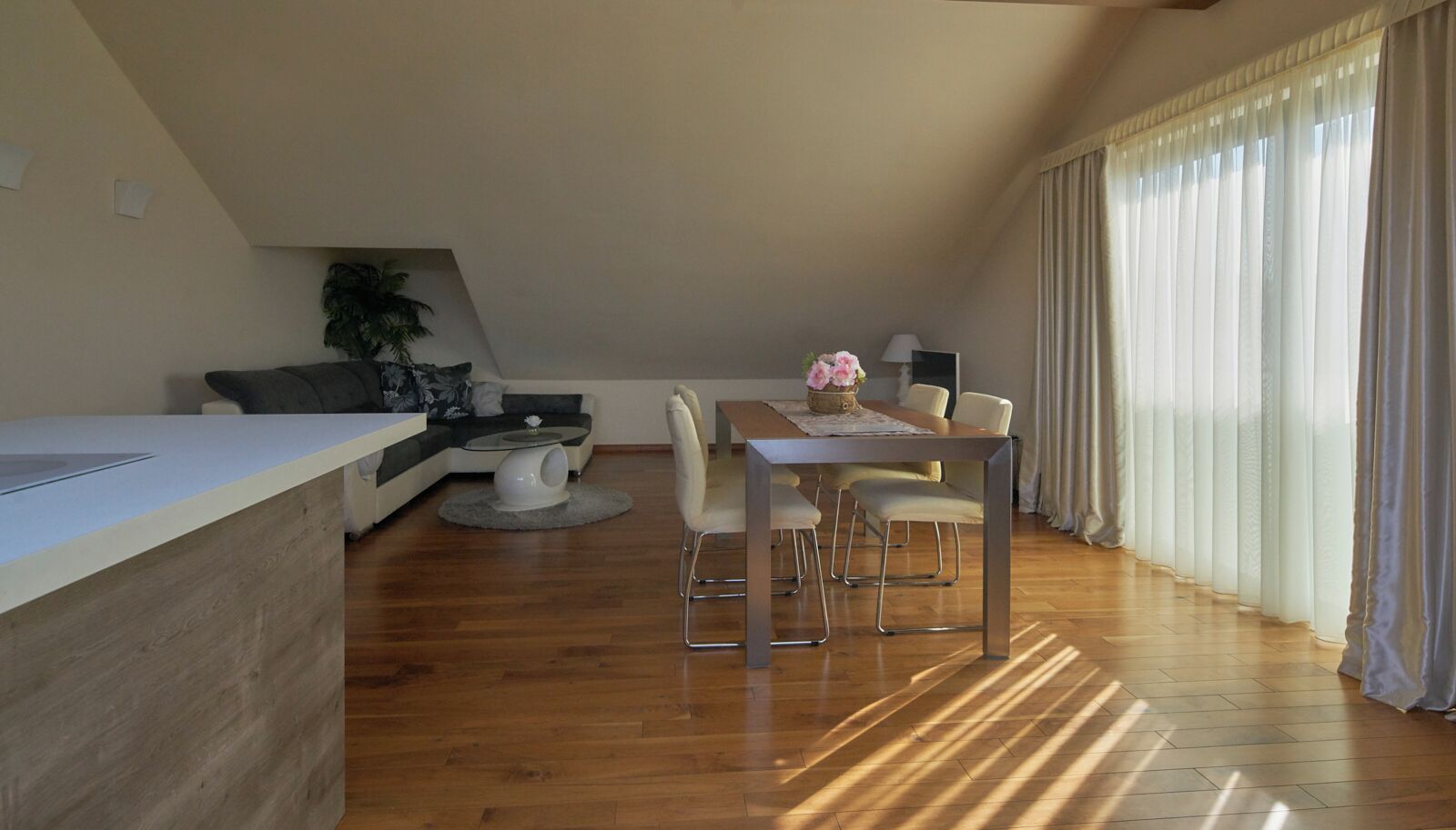 Een moderne woonkamer met een eethoek, houten vloeren, een bank, een klein rond tafeltje en een eettafel met stoelen.