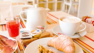 Un desayuno con croissant, café, jugo y pasteles sobre un mantel a rayas.