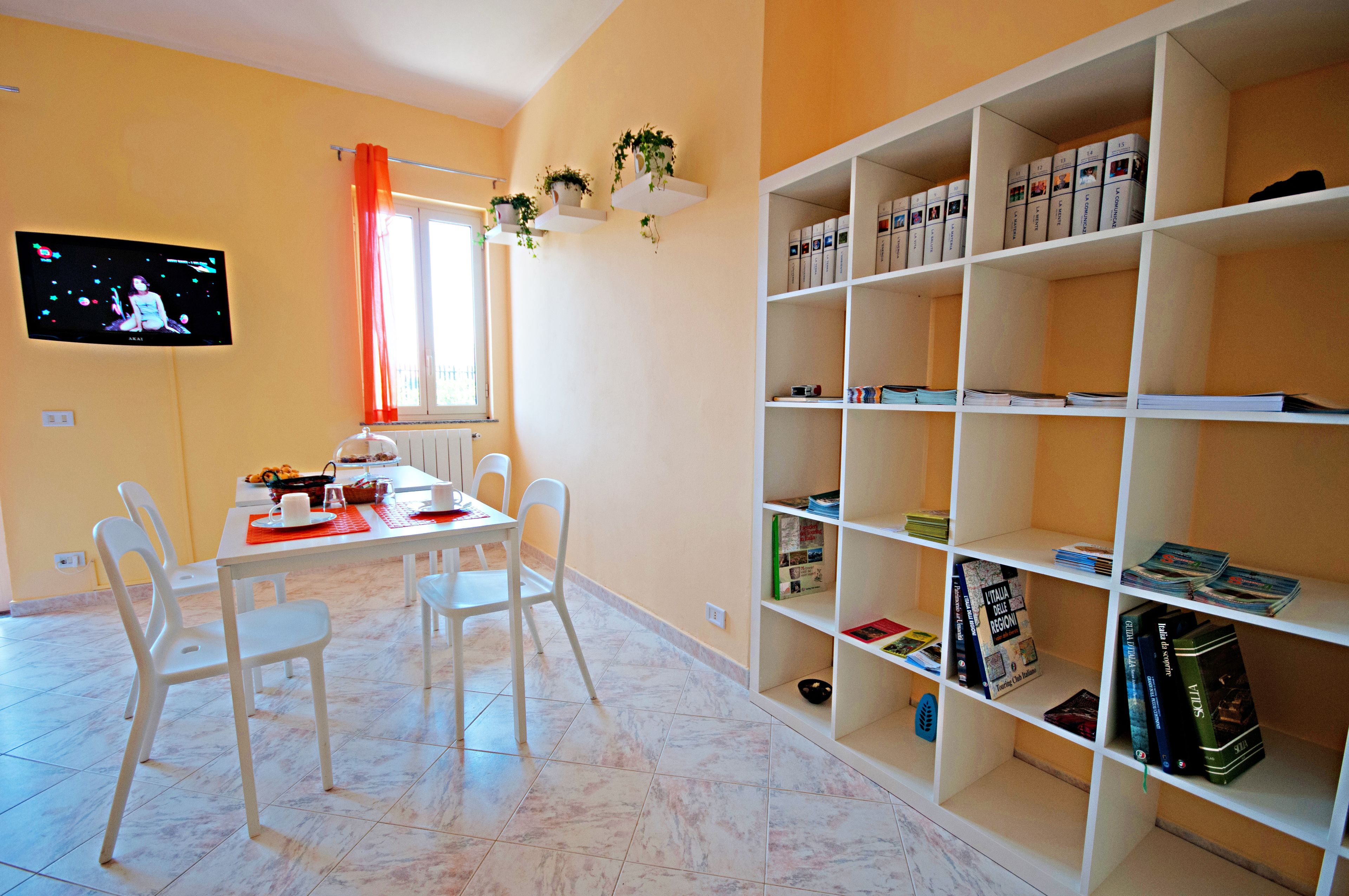 Un coin repas avec une table et des chaises, un téléviseur fixé au mur et une bibliothèque remplie de livres et d’objets décoratifs.