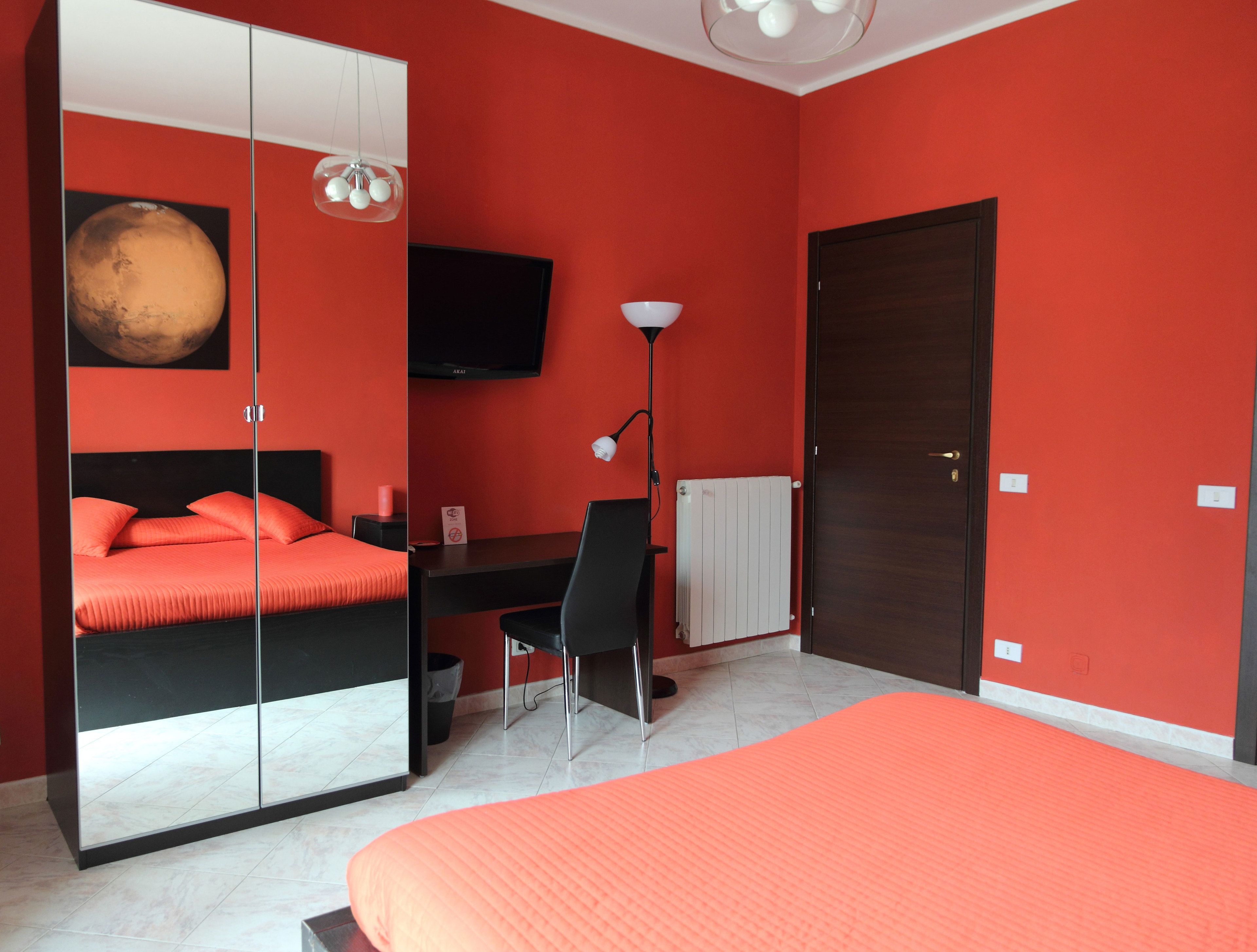 Un dormitorio con cama, escritorio, silla, armario, televisor y radiador.