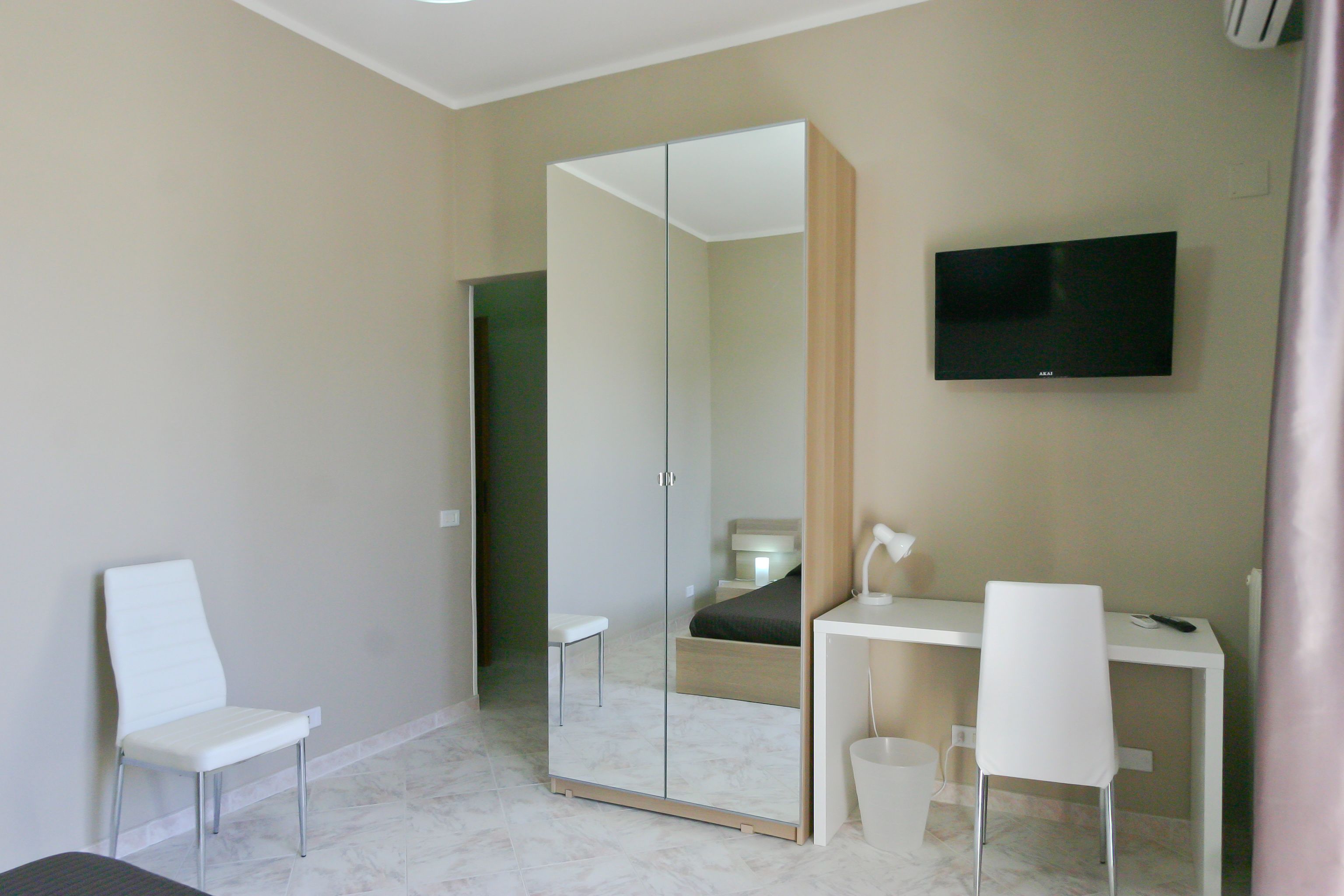 A modern bedroom with a large mirror, a bed, a desk, and a TV.