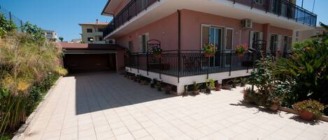 A multi-story residential building with a tiled patio, potted plants, and a fenced area.