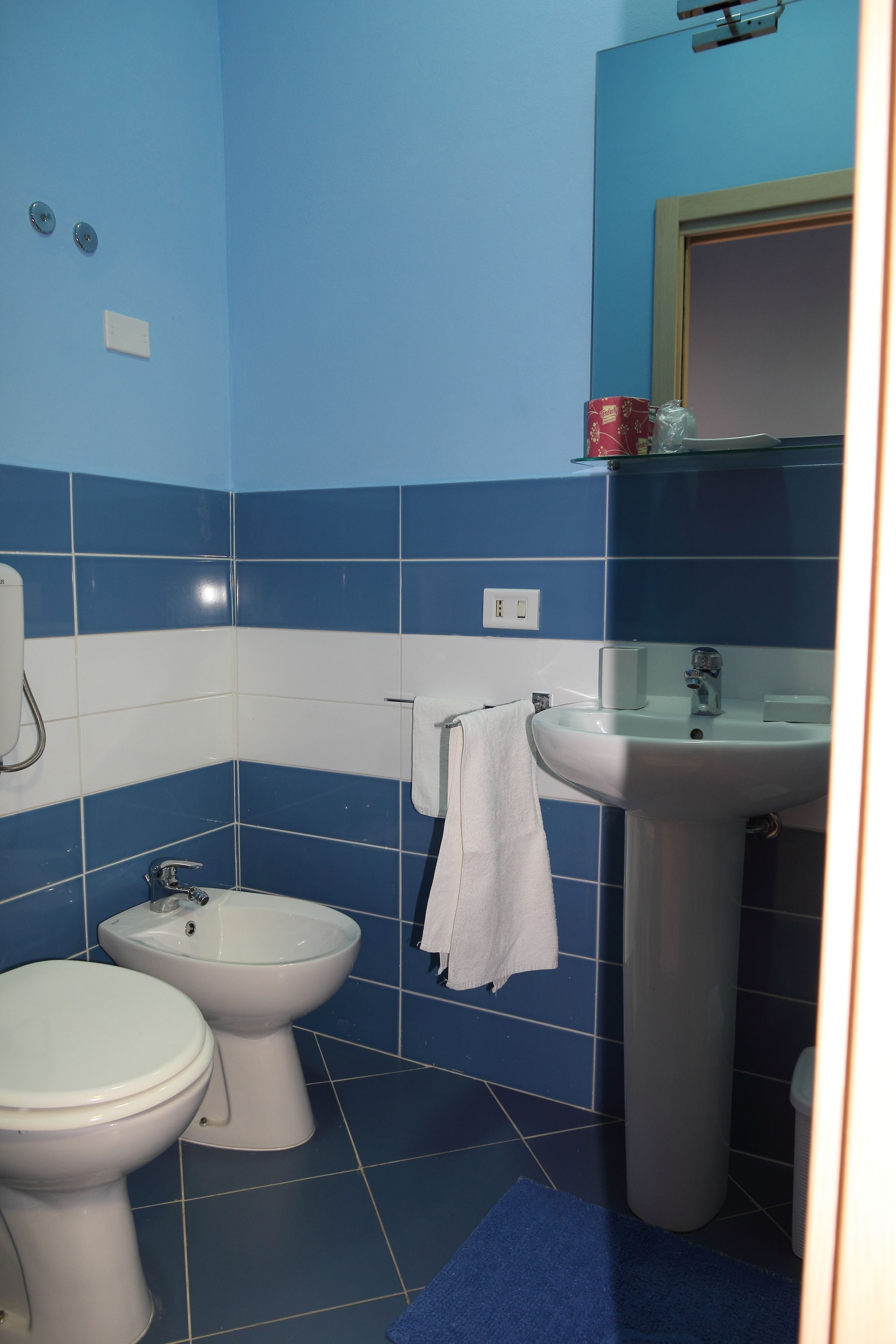 Een badkamer met blauwe en witte tegels, een wit wastafelmeubel, een bidet en een toilet.