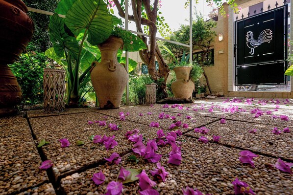 A garden area with large vases, a rooster sign, and scattered flower petals on a tiled floor.