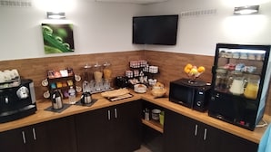 Angolo cottura con macchine da caffè, forno a microonde, frigorifero e diversi alimenti.