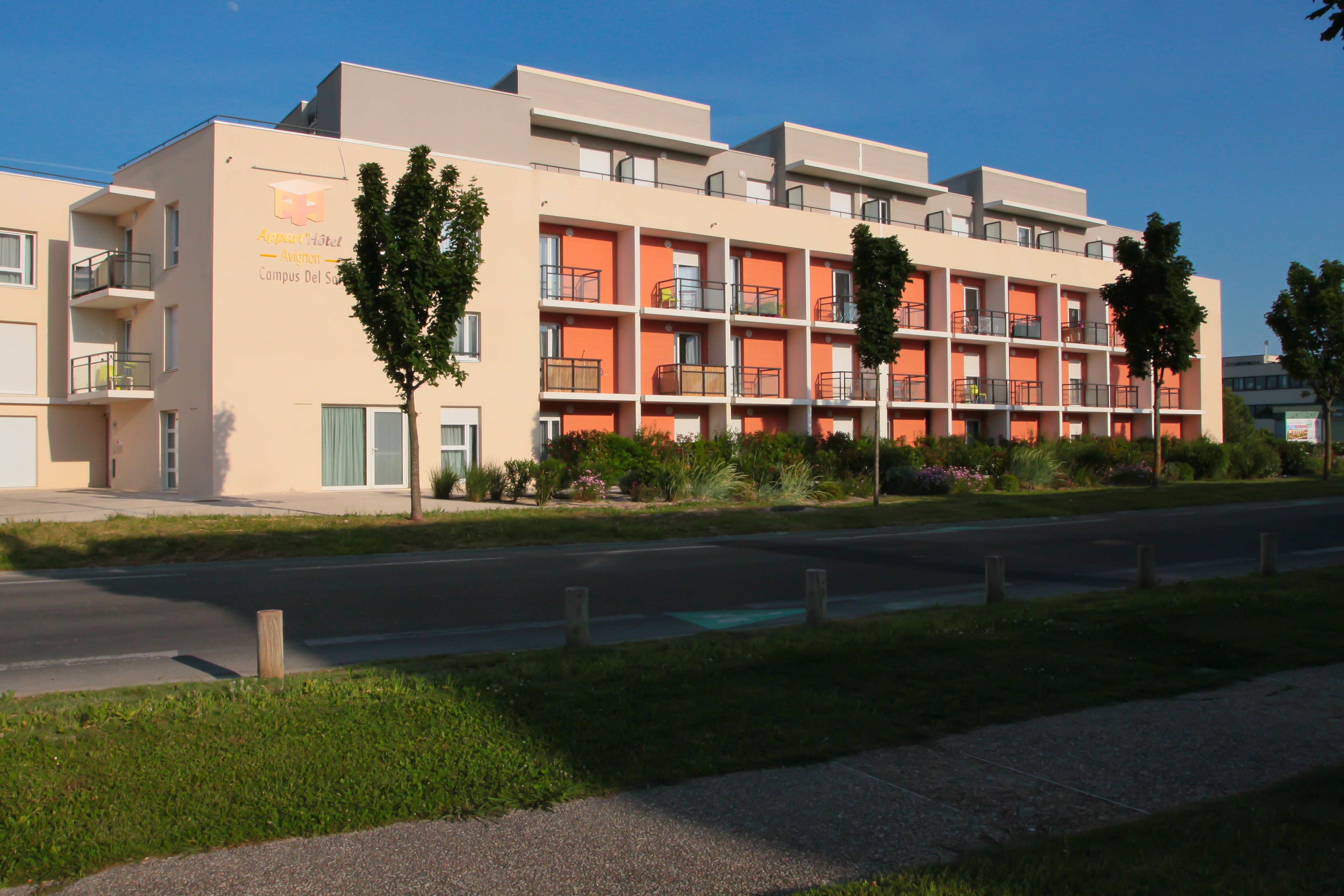 A multi-story hotel with balconies, a parking lot, and a well-maintained lawn.