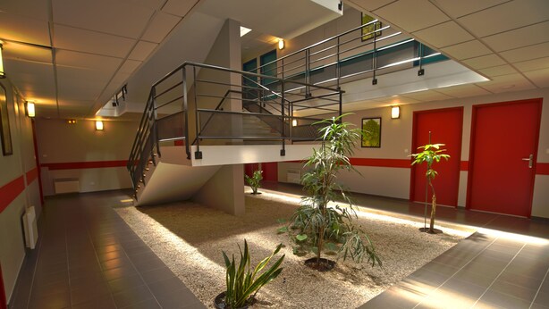 Un'ampia hall con una moderna scala, pavimento piastrellato e piante in vaso.