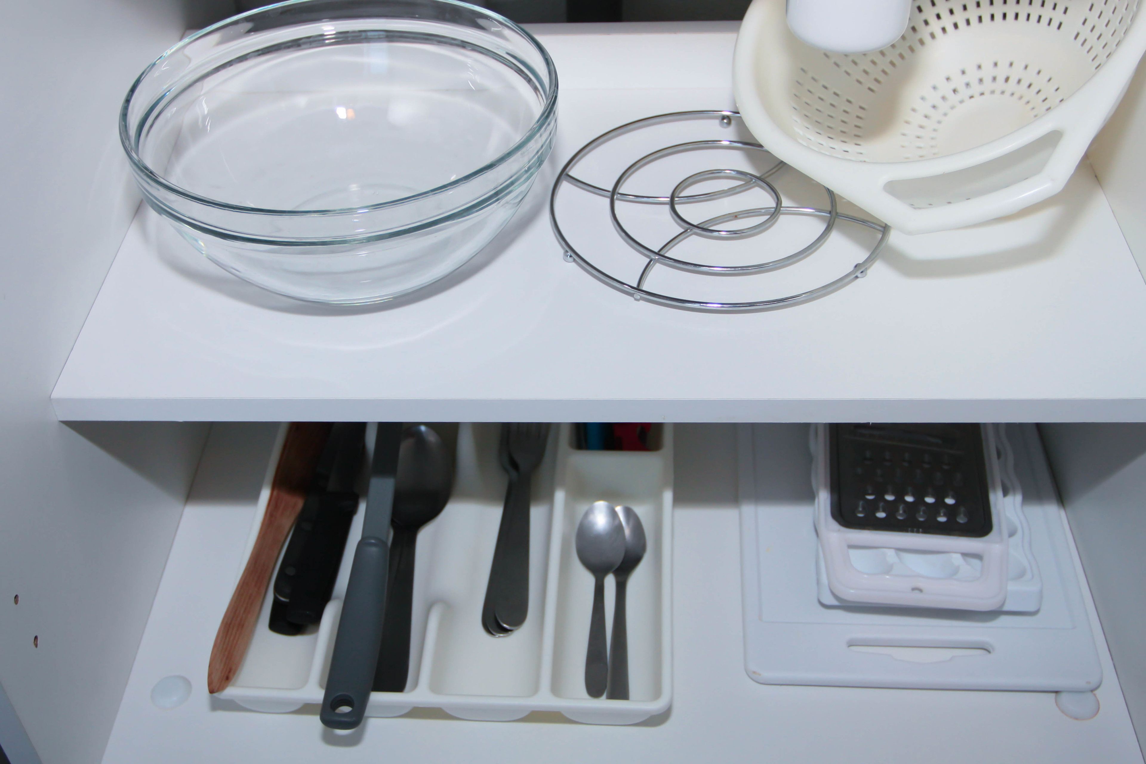 Una encimera de cocina con un bol de vidrio, un colador y un recipiente para utensilios.