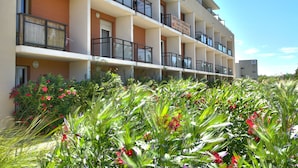 Un hotel a più piani con balconi, un'area giardino con fiori rossi e un cielo sereno.