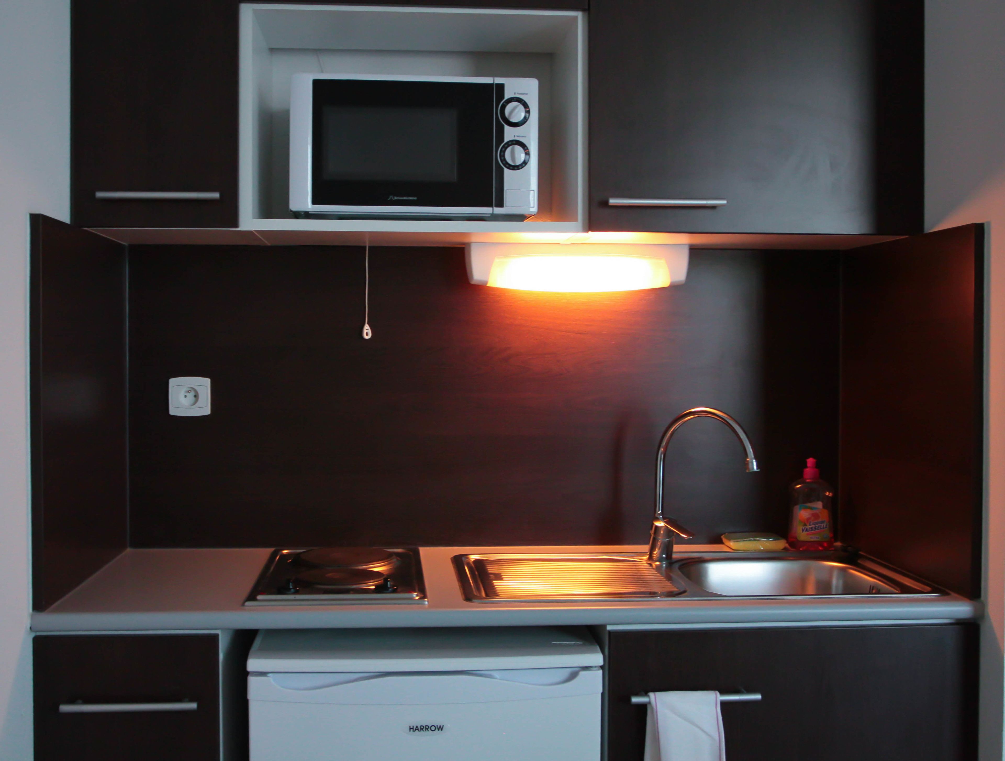 A compact kitchen with a microwave, stove, sink, and a small refrigerator.