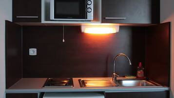 A compact kitchen with a microwave, stove, sink, and a small refrigerator.