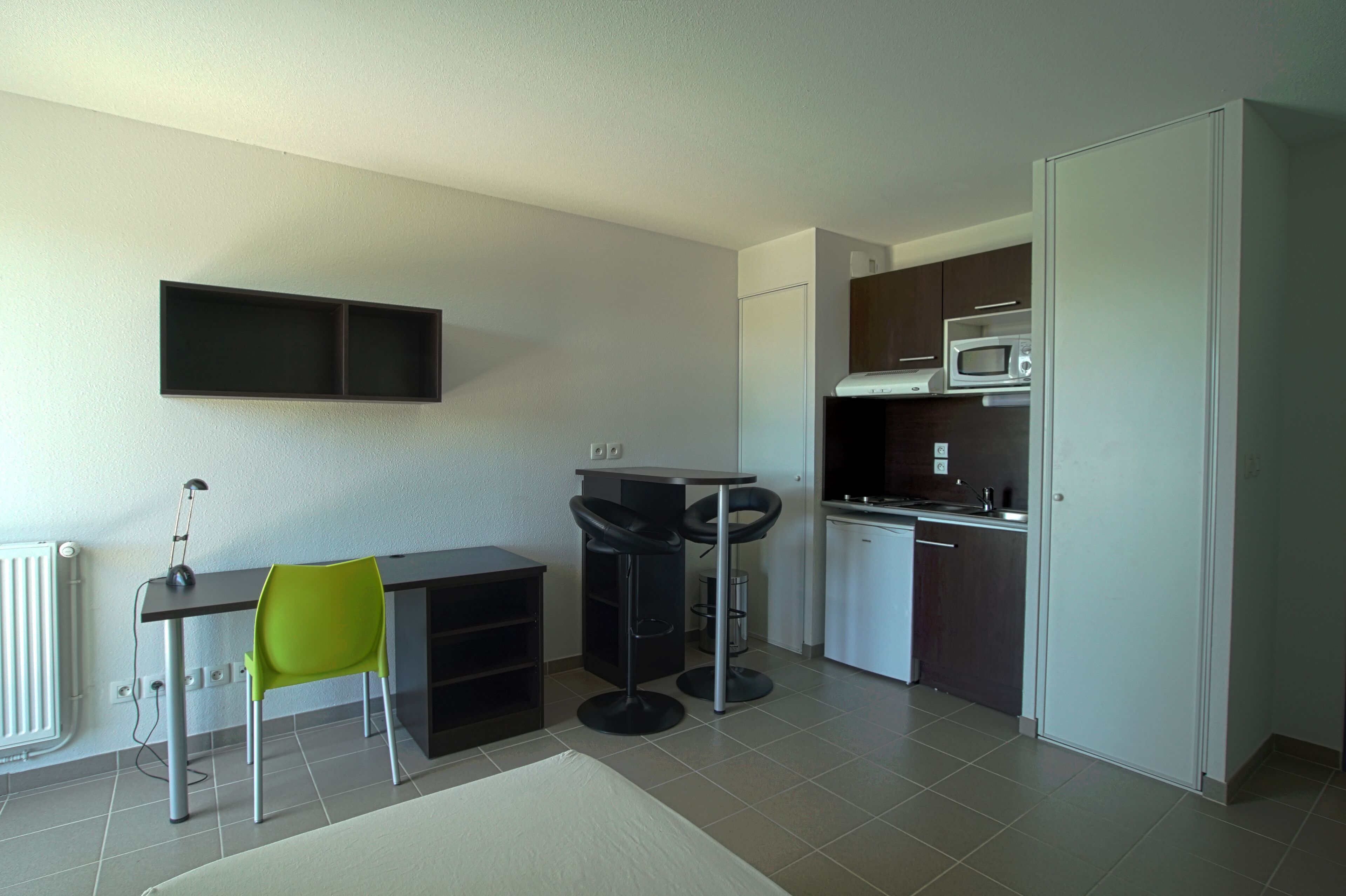 Een kleine keuken met een magnetron, fornuis en kastjes. Er is een eethoek met een tafel en twee stoelen.