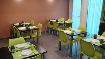 Un comedor con mesas y sillas, una cafetera y un ventanal con cortinas.