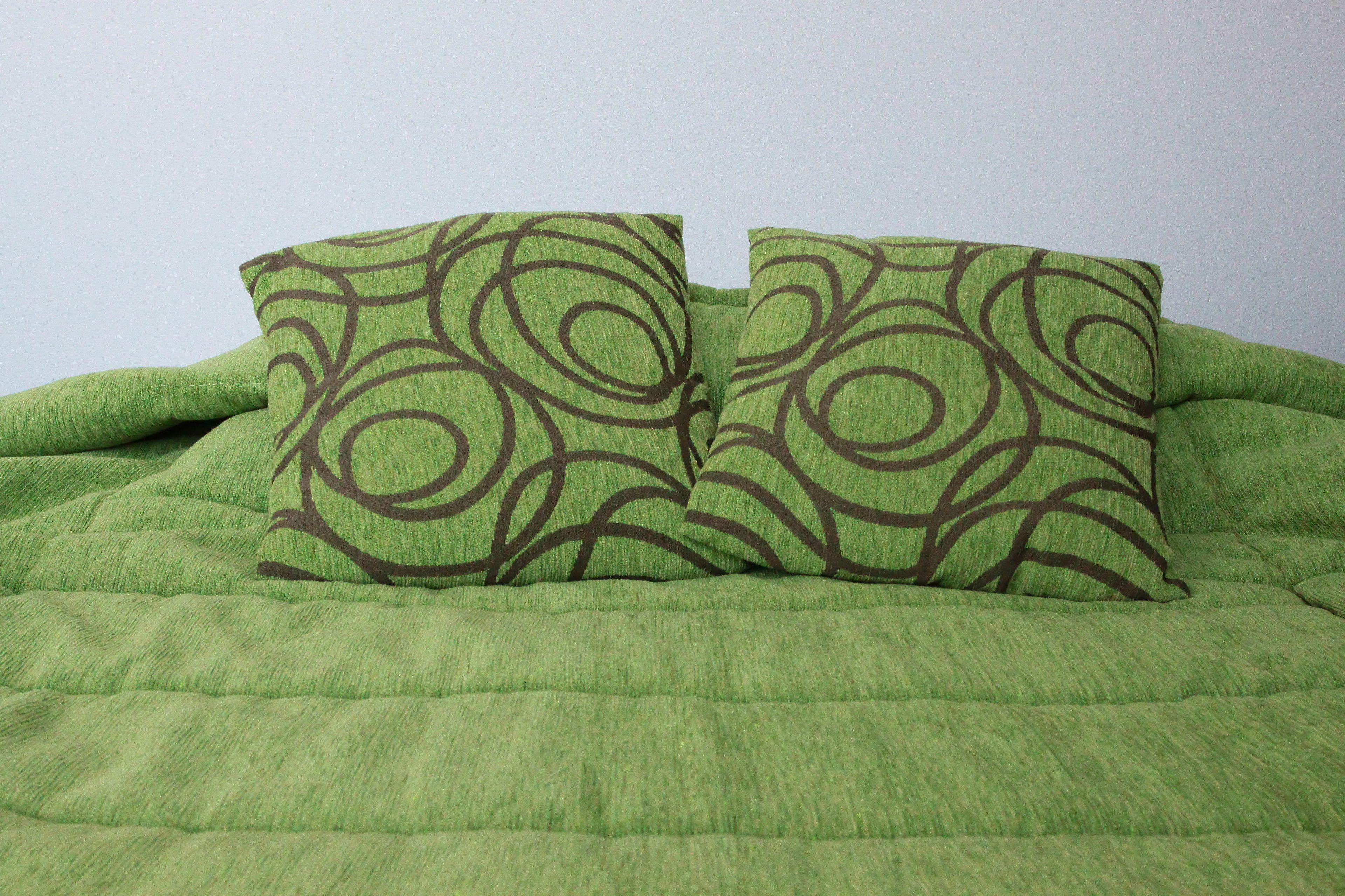 A bed with a green quilt and two pillows with a circular pattern.