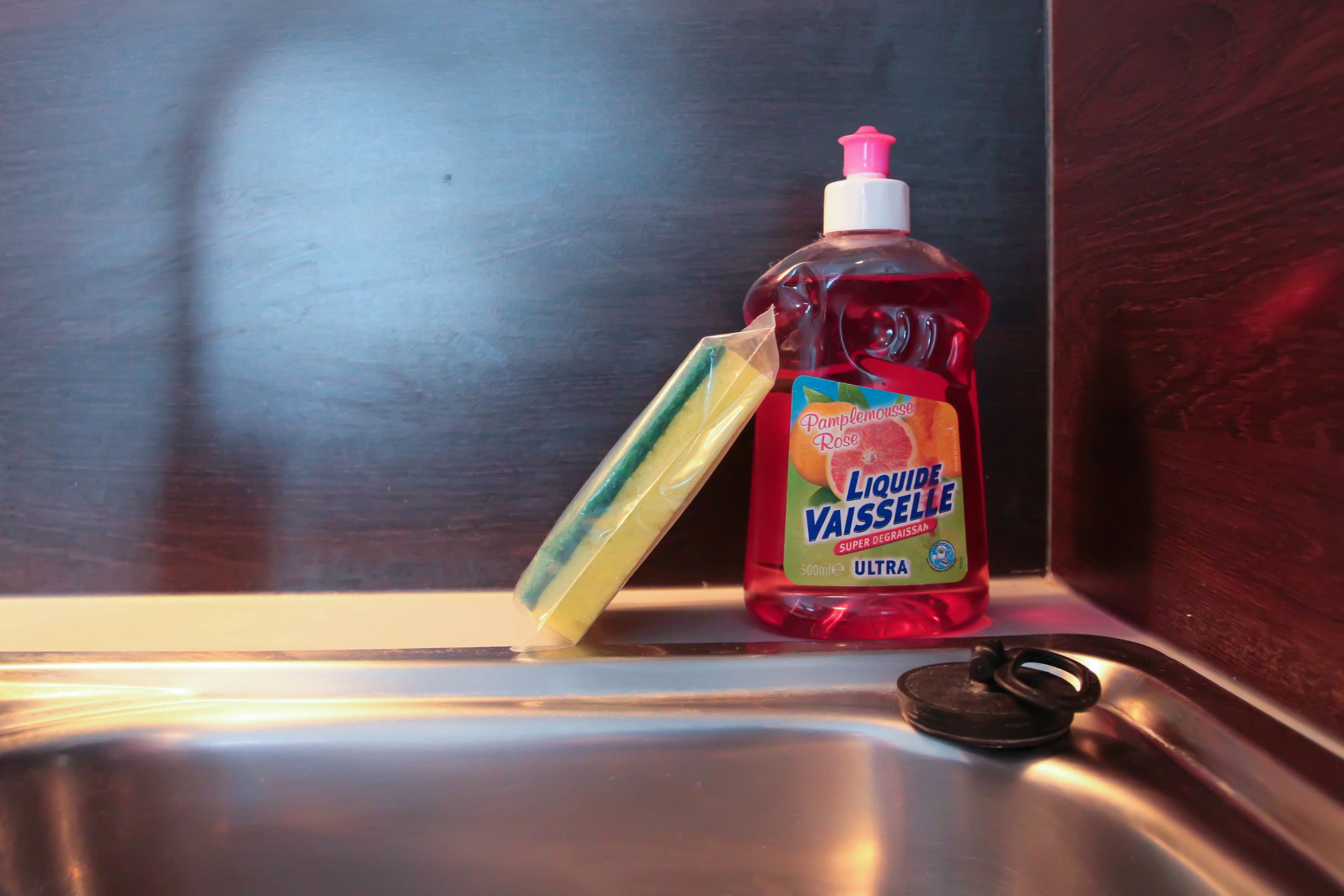 A bottle of liquid dish soap and a sponge in a kitchen sink.