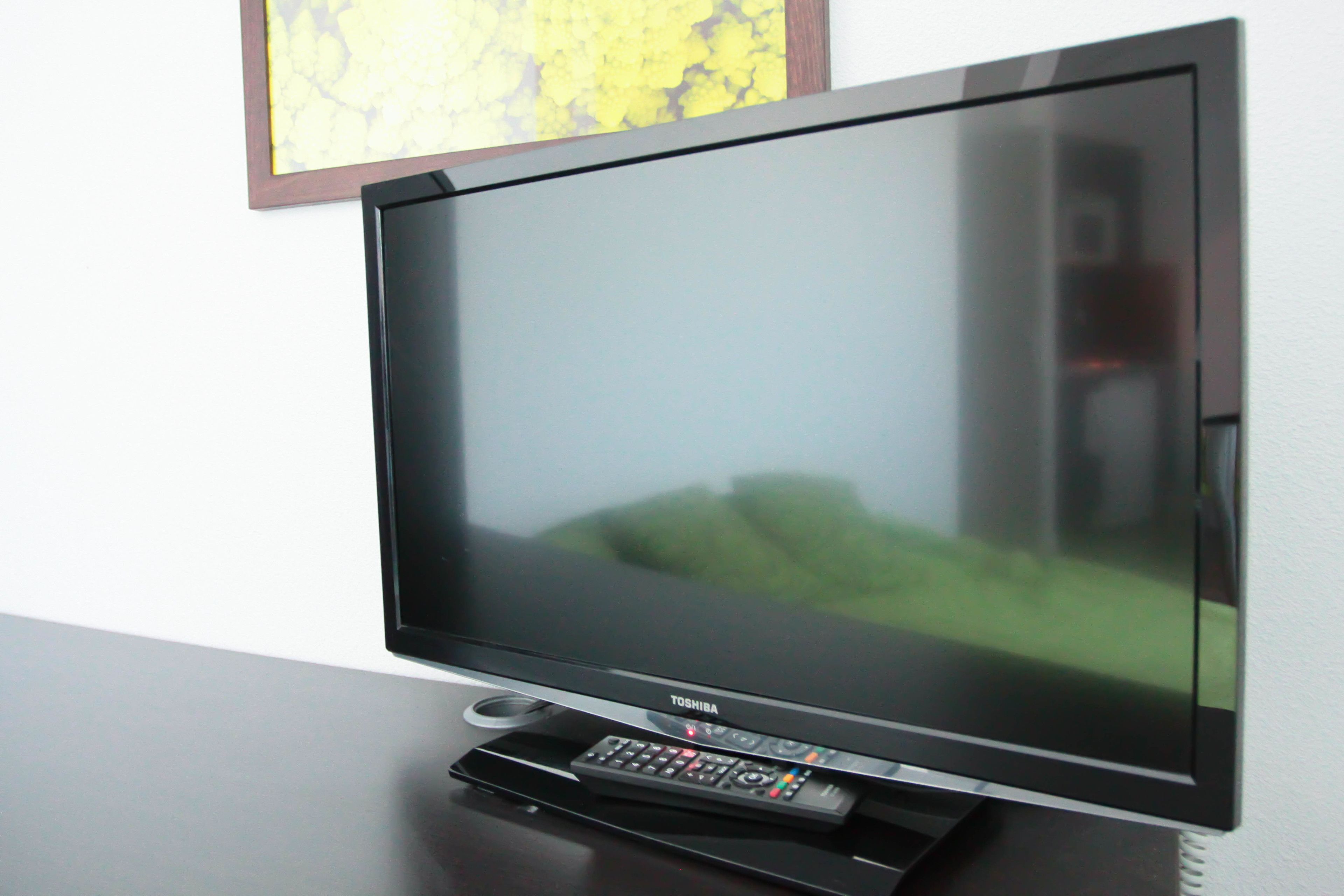 Ein Flachbildfernseher auf einem Ständer mit Fernbedienung, an der Wand befestigt.