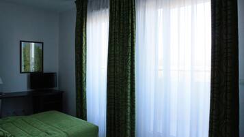 Una habitación de hotel con una cama, un escritorio con televisor y cortinas translúcidas.