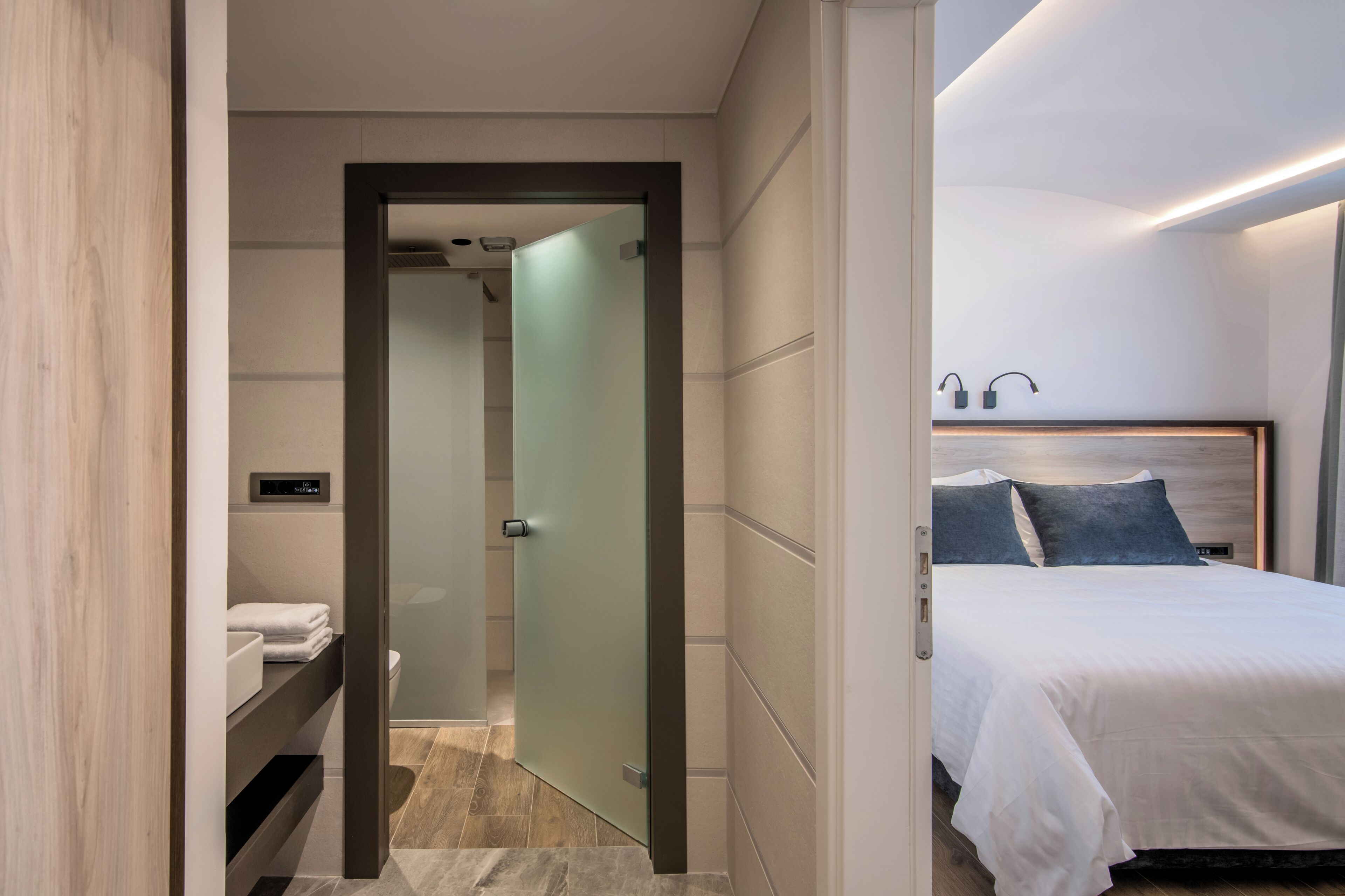 A modern hotel room with a bed, a nightstand, a bathroom with a toilet, and a shower area.