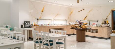 Un comedor moderno con paredes de mármol, una barra de buffet y mobiliario blanco.
