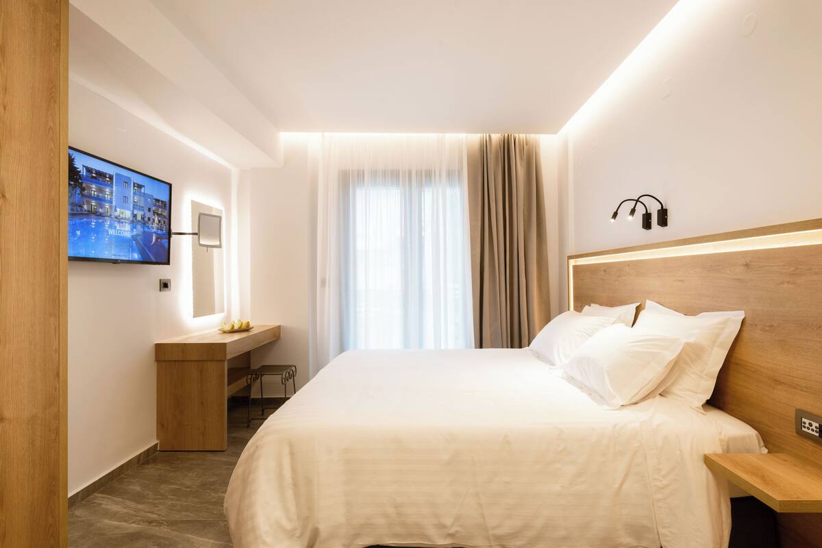 A hotel room with a bed, a desk, a TV, and a window with curtains.