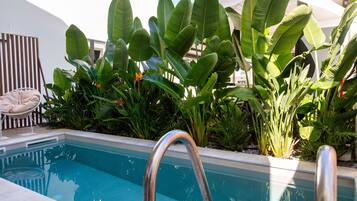 A swimming pool with a metal ladder, surrounded by lush tropical plants and a white chair.