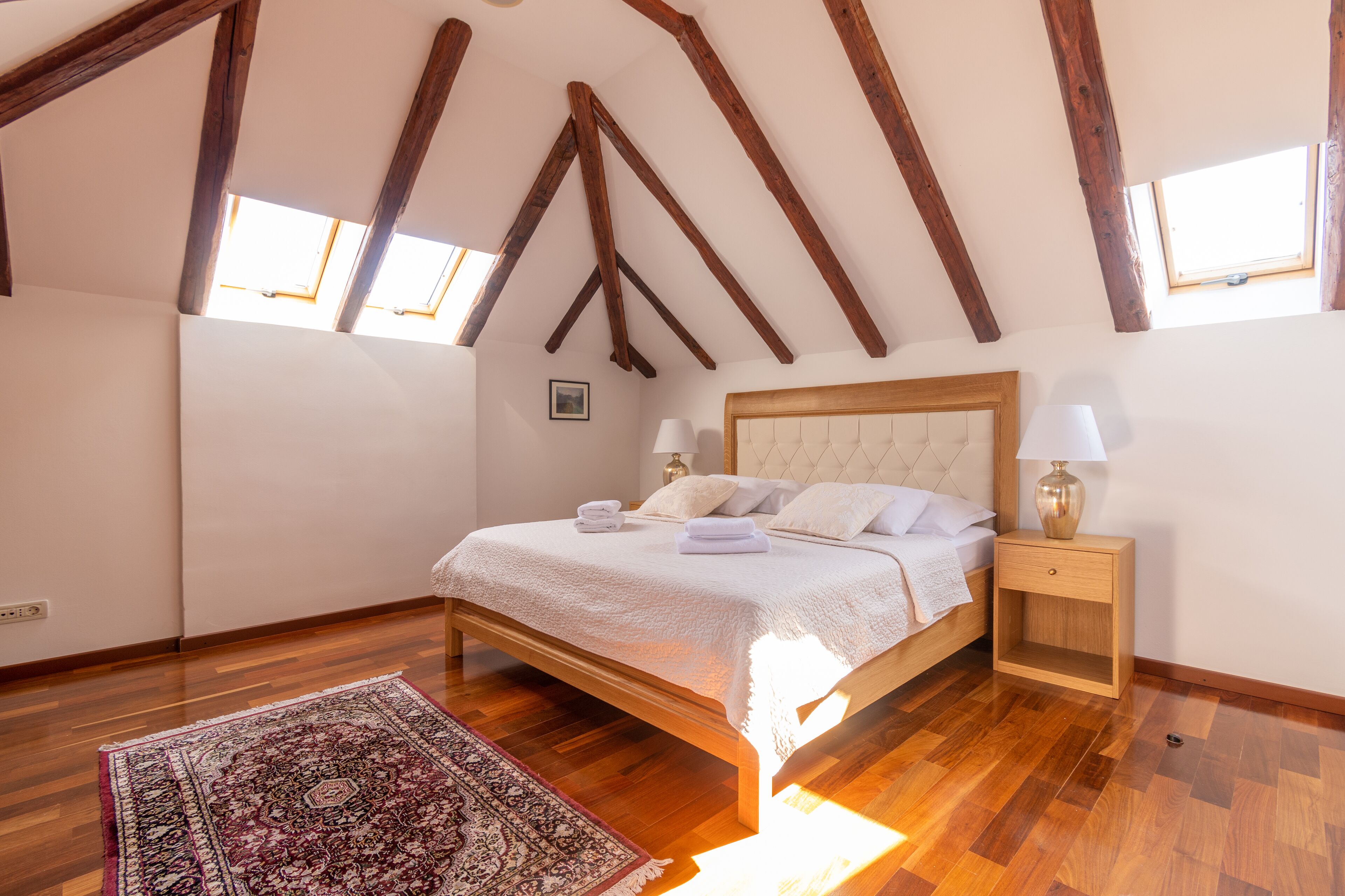 Una camera da letto con un letto di legno, un comodino, un tavolino e un tappeto, oltre a una finestra.